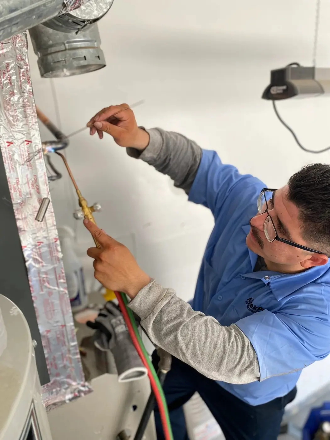 AirtekPros technician brazing a connection at an indoor air handler and duct plenum