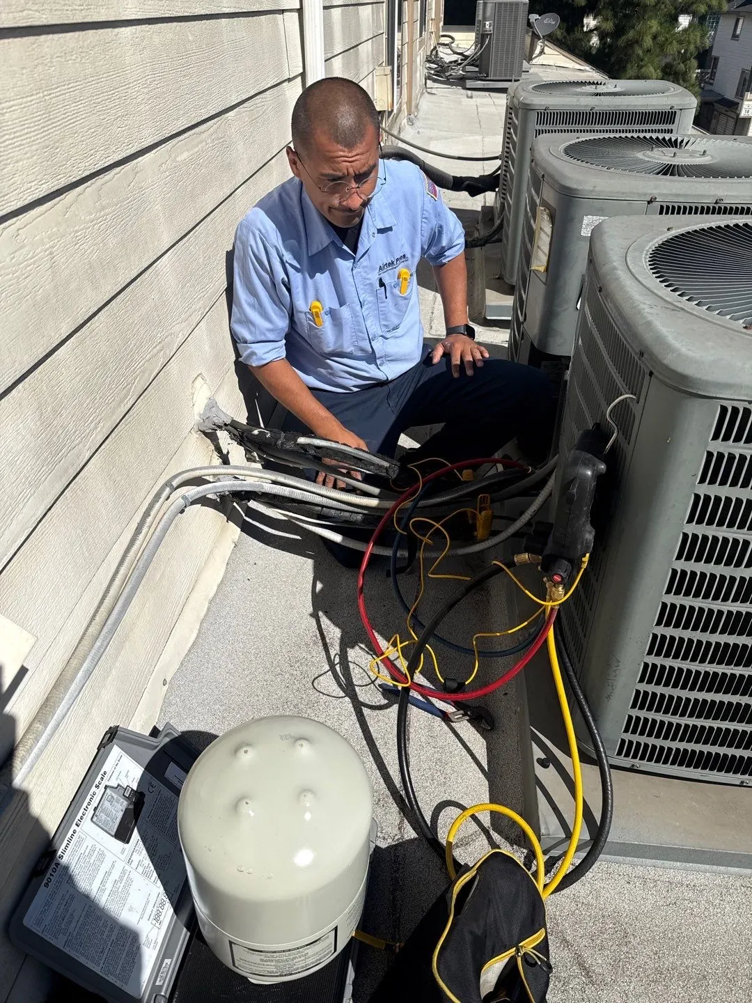 AirtekPros technician testing the electrical panel of an outdoor condensing unit with test leads and a service manual