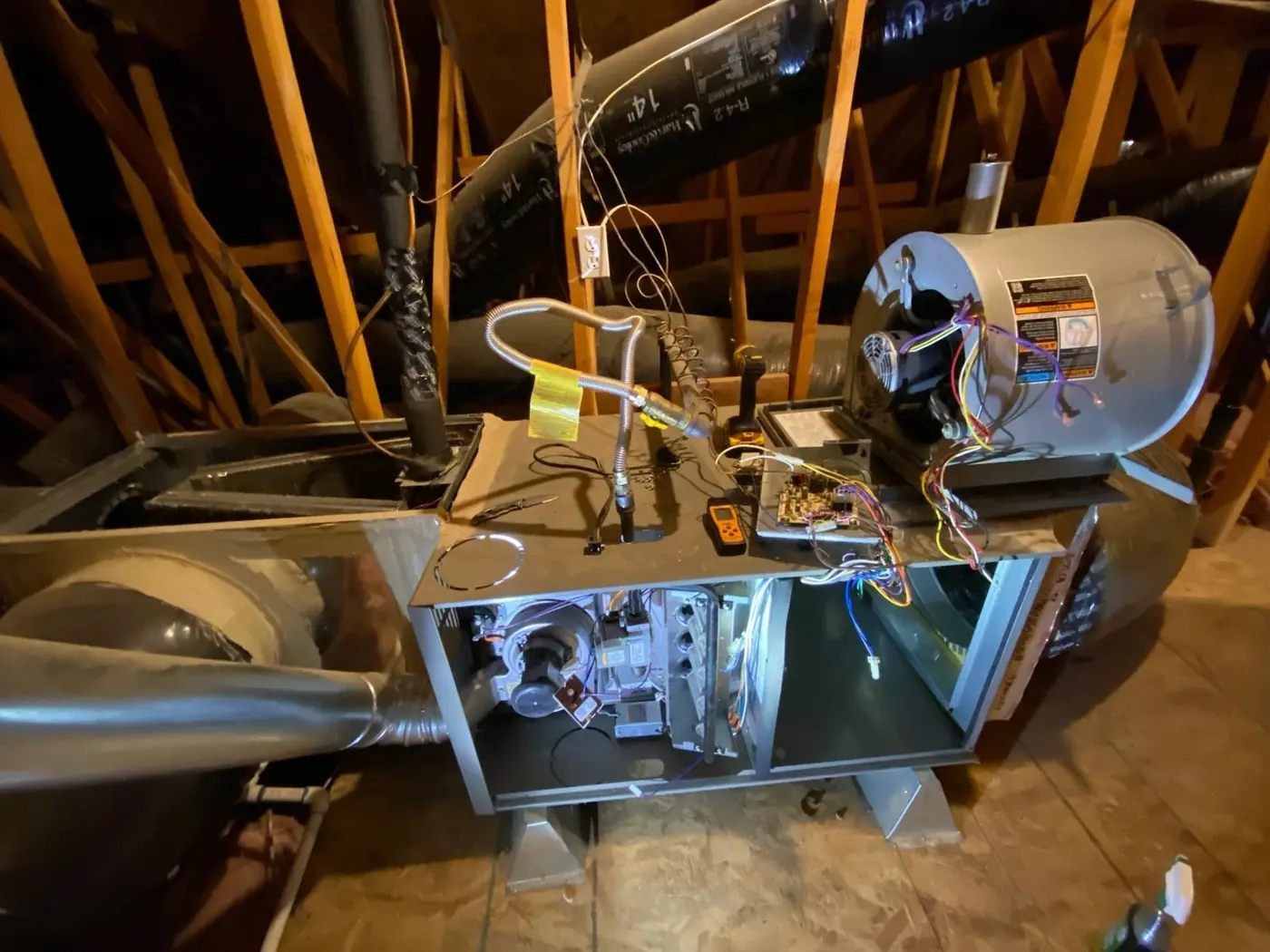 Open air handler in an attic with test leads and a meter connected during a diagnostic