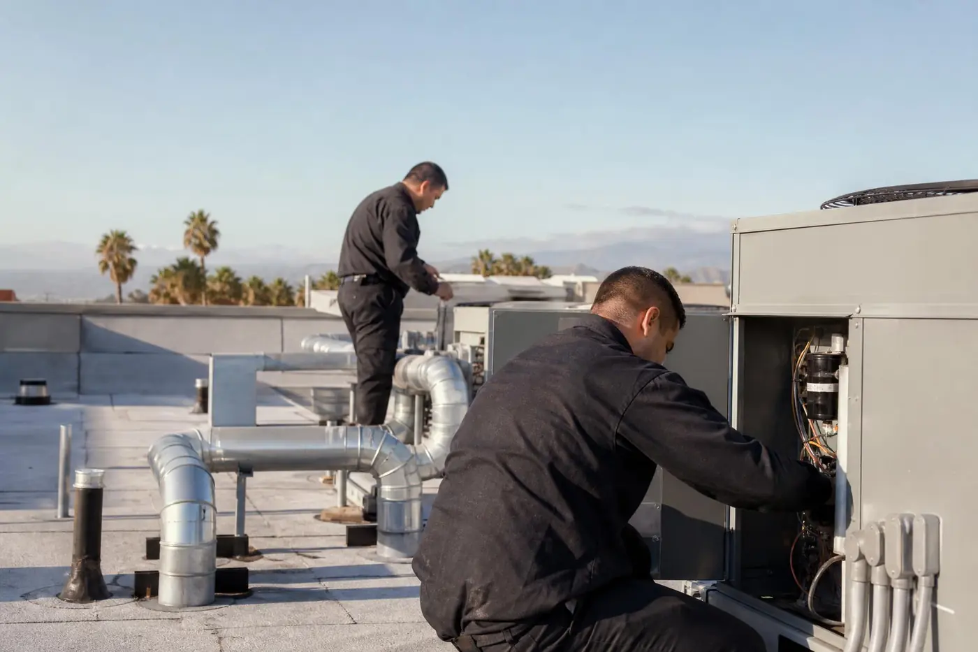 Two technicians servicing rooftop packaged units on a light commercial building
