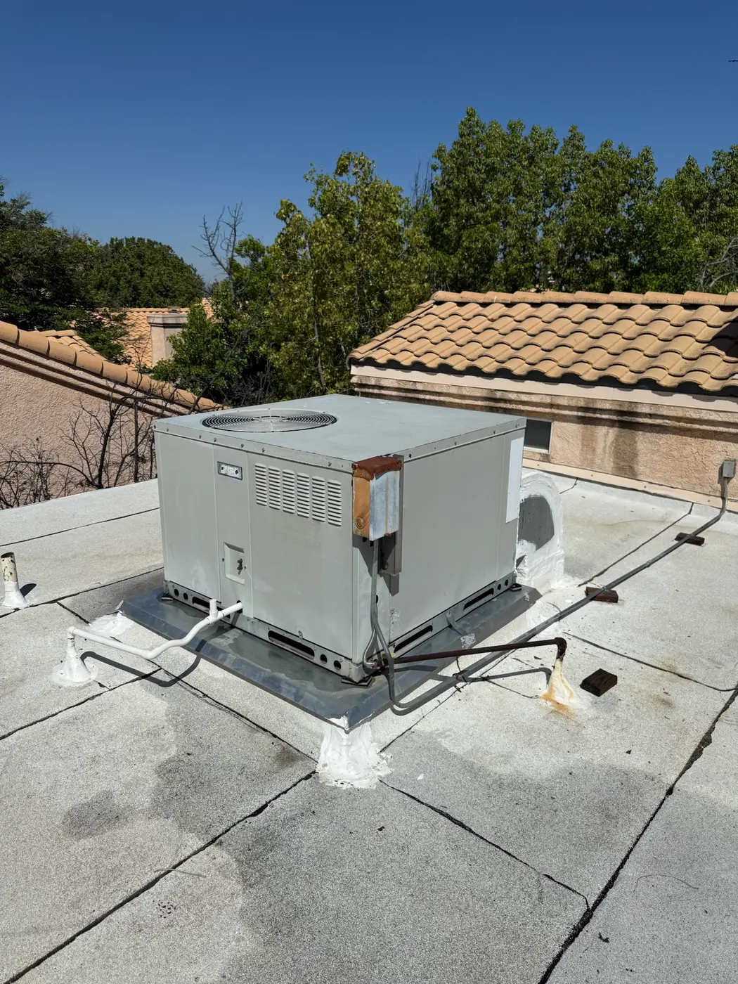 Packaged rooftop HVAC unit installed on a flat roof next to tile roofing